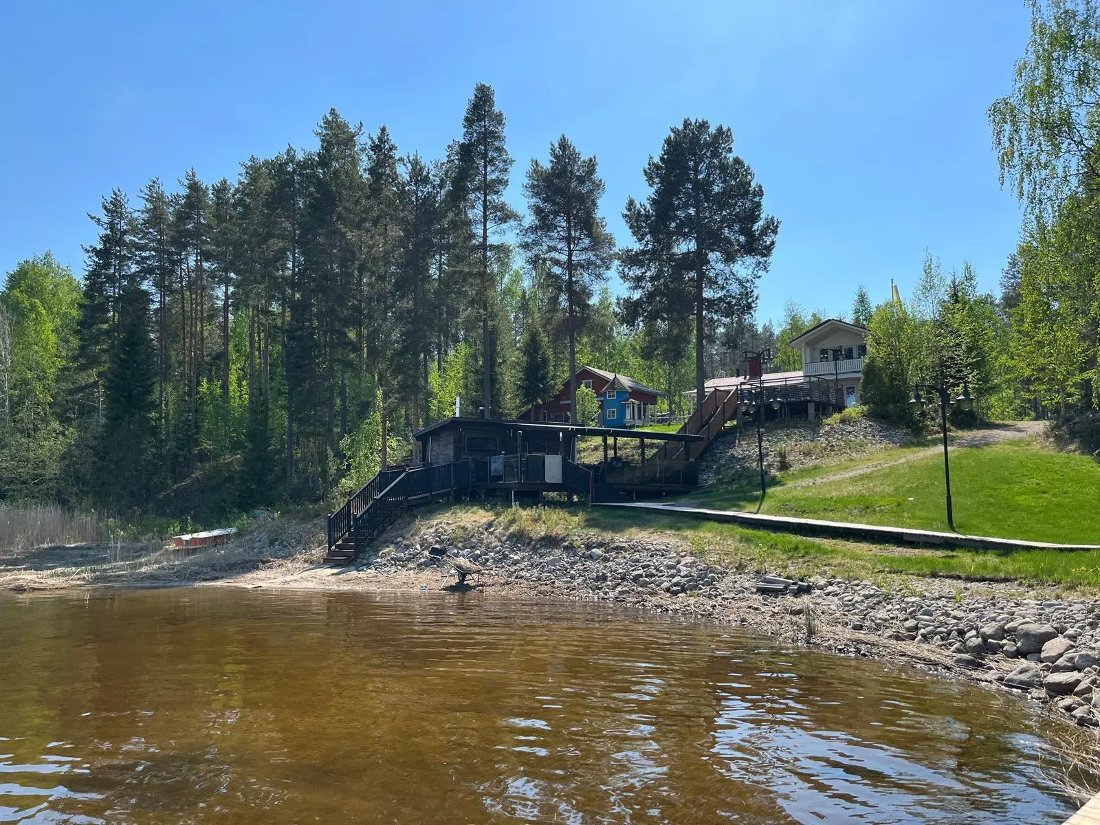 Kokonaisnäkymä vedestä: rantasauna, huvila ja järvi