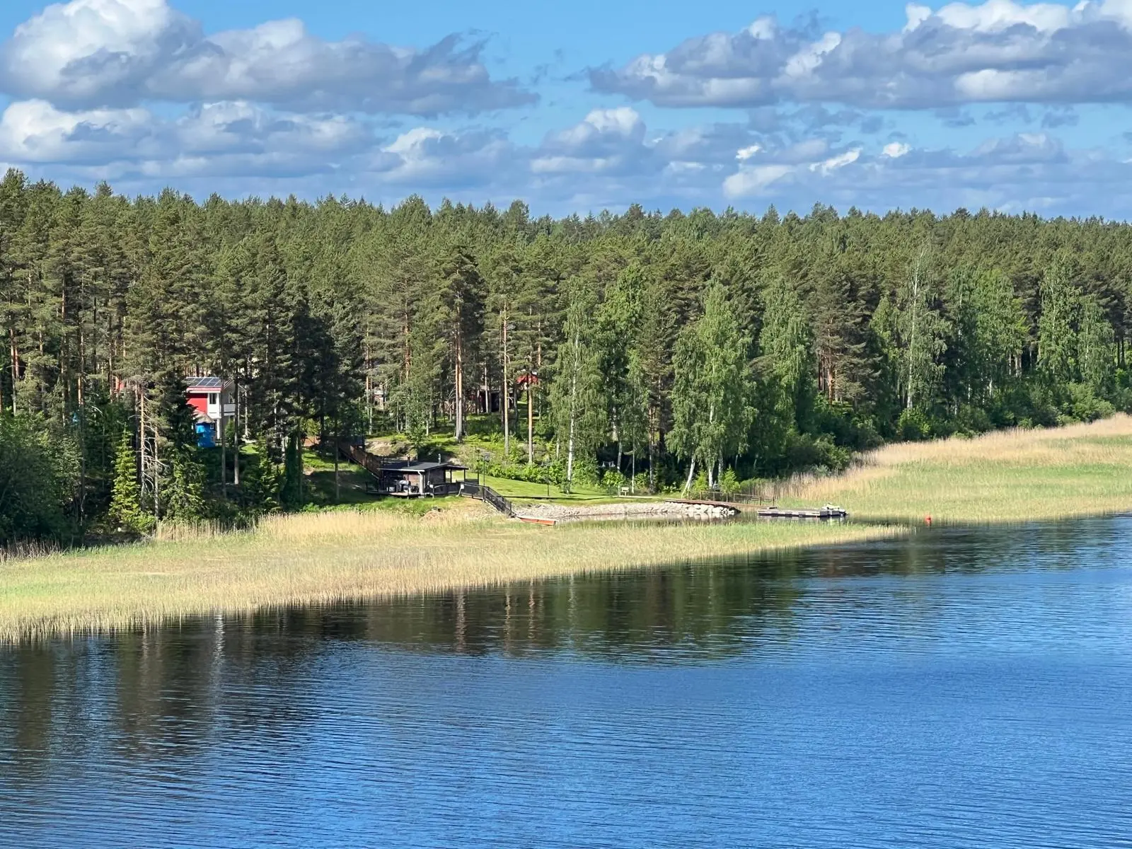 Villa Purnukan rantanäkymä järveltä, rantasauna ja aitta puiden lomassa